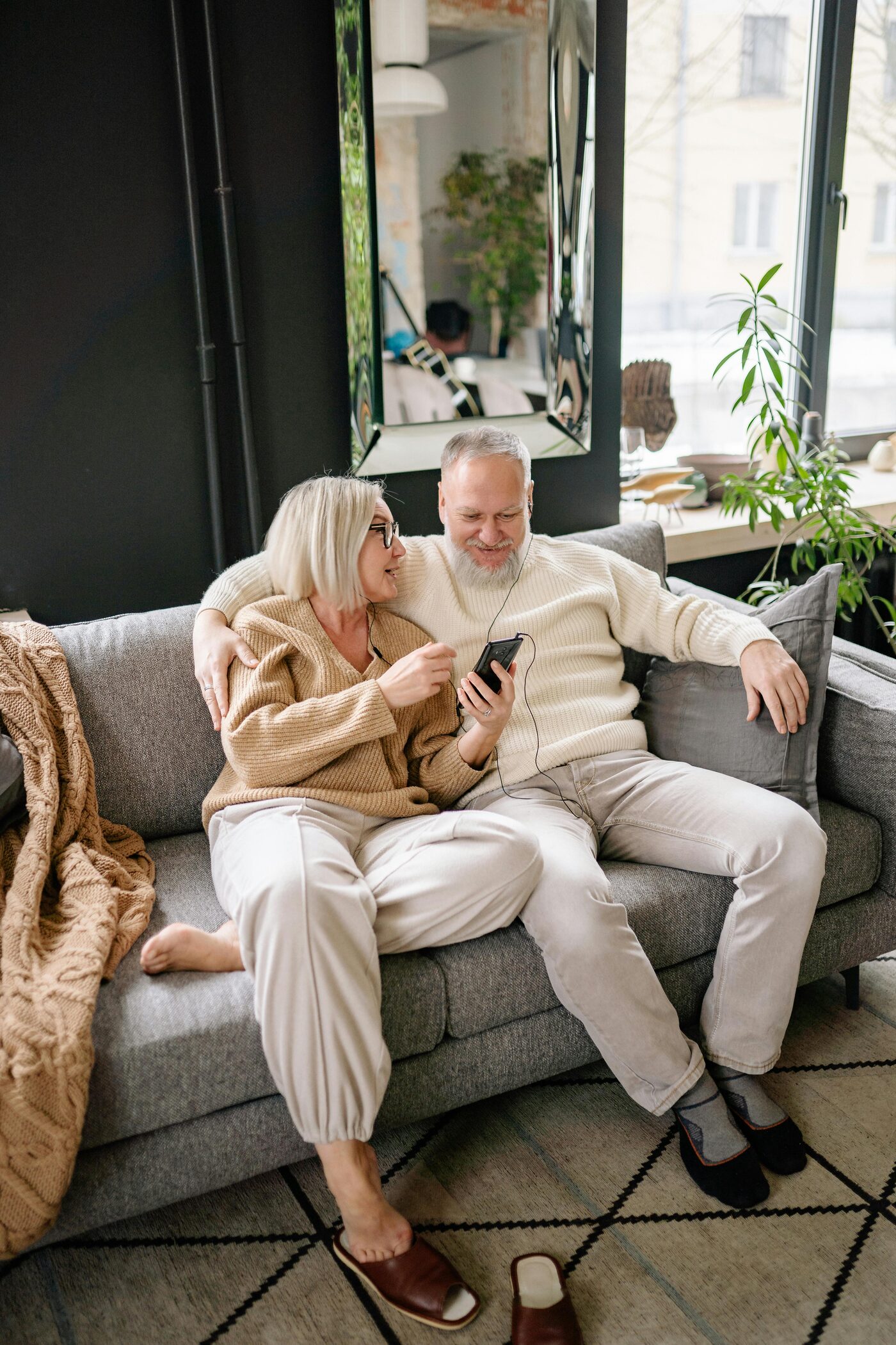 A couple sitting together on a sofa, sharing earphones as they listen to their will being read back.